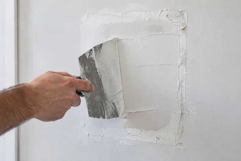 Joint compound being smoothed over a drywall patch